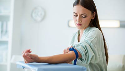 Девушка сидит за медицинским столом со жгутом на руке